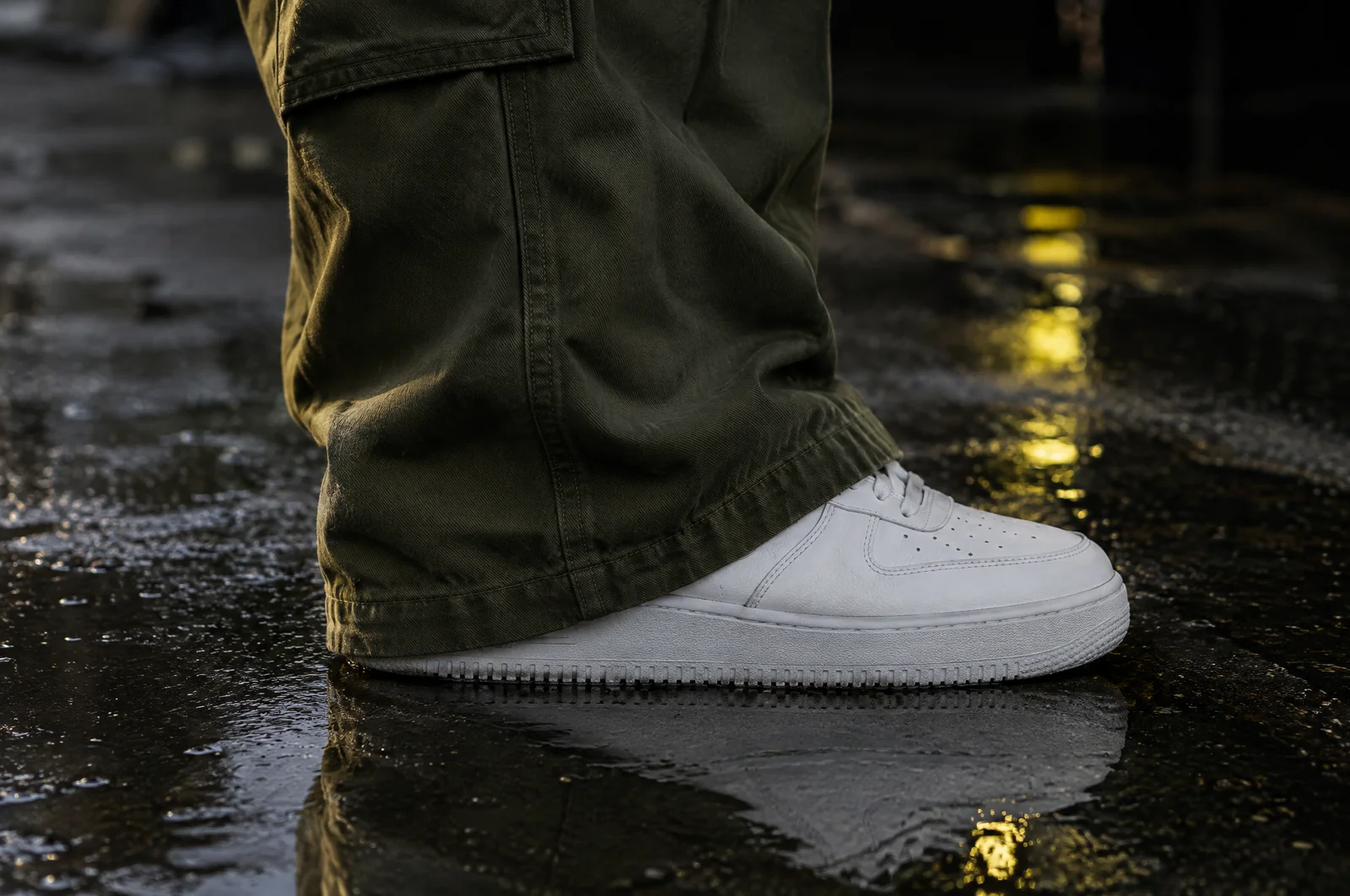 Der Saum einer weiten Cargohose liegt sauber oben auf einem weißen Sneaker, nah am Boden fotografiert.