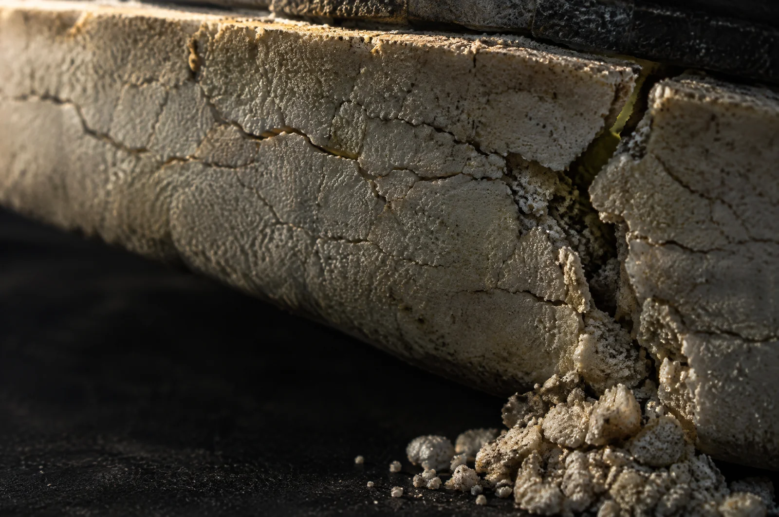Makroaufnahme einer hellen Schaumsohle im Streiflicht, von feinen Rissen durchzogen, an der Bruchkante rieseln Krümel heraus.